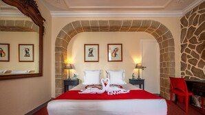 A hotel room with a large bed, a stone archway, two framed pictures on the wall, and a red chair. - Logis Auberge de Kerveoc'h (Douarnenez)