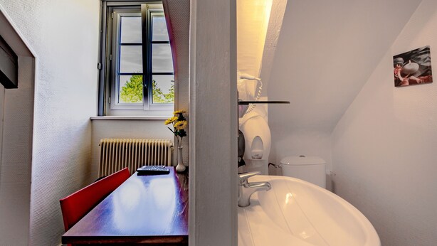 A bathroom with a white sink, a window with a view, and a red chair. - Logis Auberge de Kerveoc'h (Douarnenez)