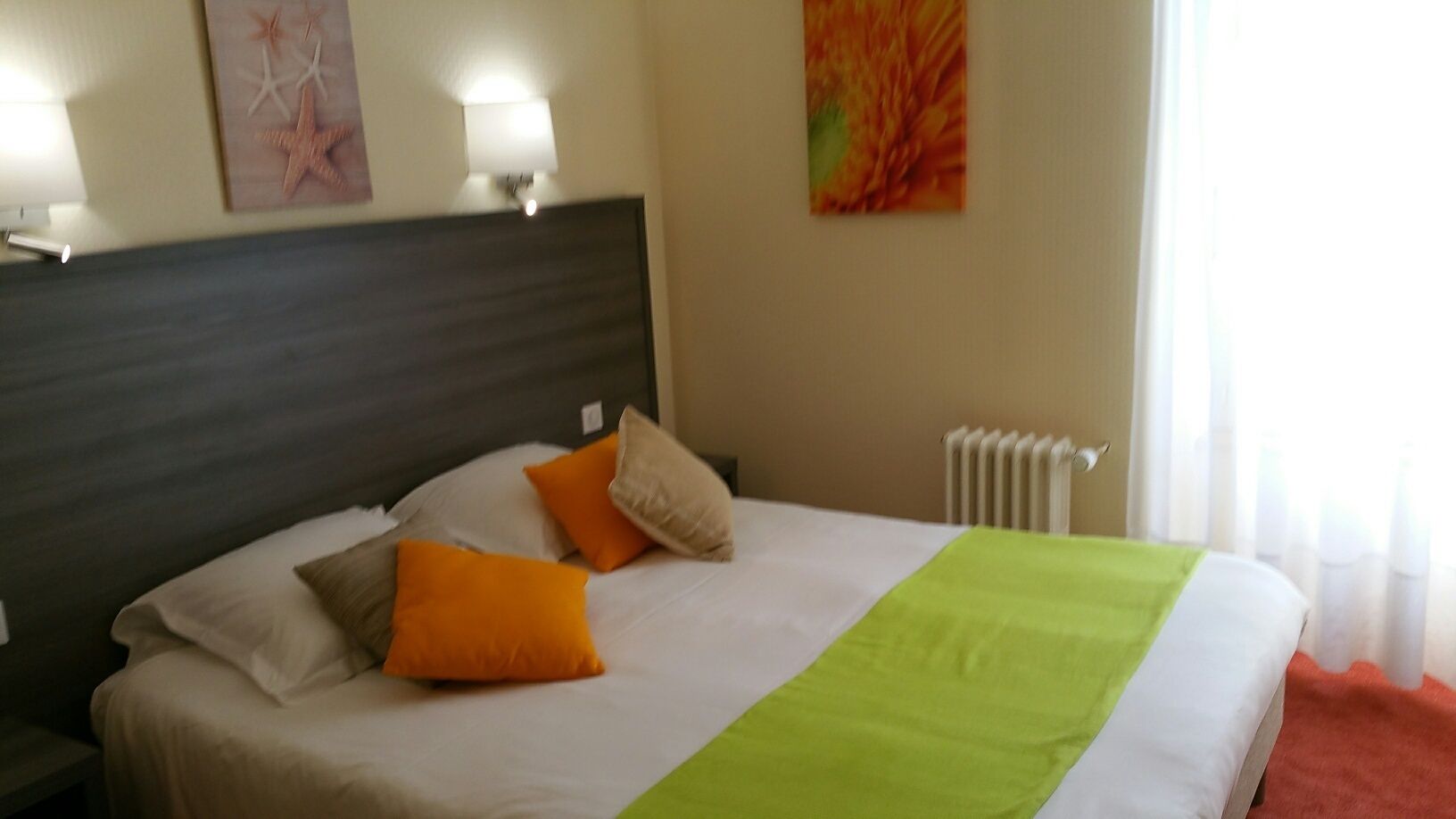 Un lit bien fait, recouvert d’une couvre-lit verte et blanche, avec deux oreillers orange et une tête de lit sombre.
