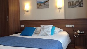 A hotel room with a bed, a wardrobe, two wall-mounted lights, and two paintings. - Citotel Du Port Rhu (Douarnenez)