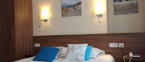 Una habitación de hotel con una cama, un armario, dos lámparas de pared y dos cuadros.
