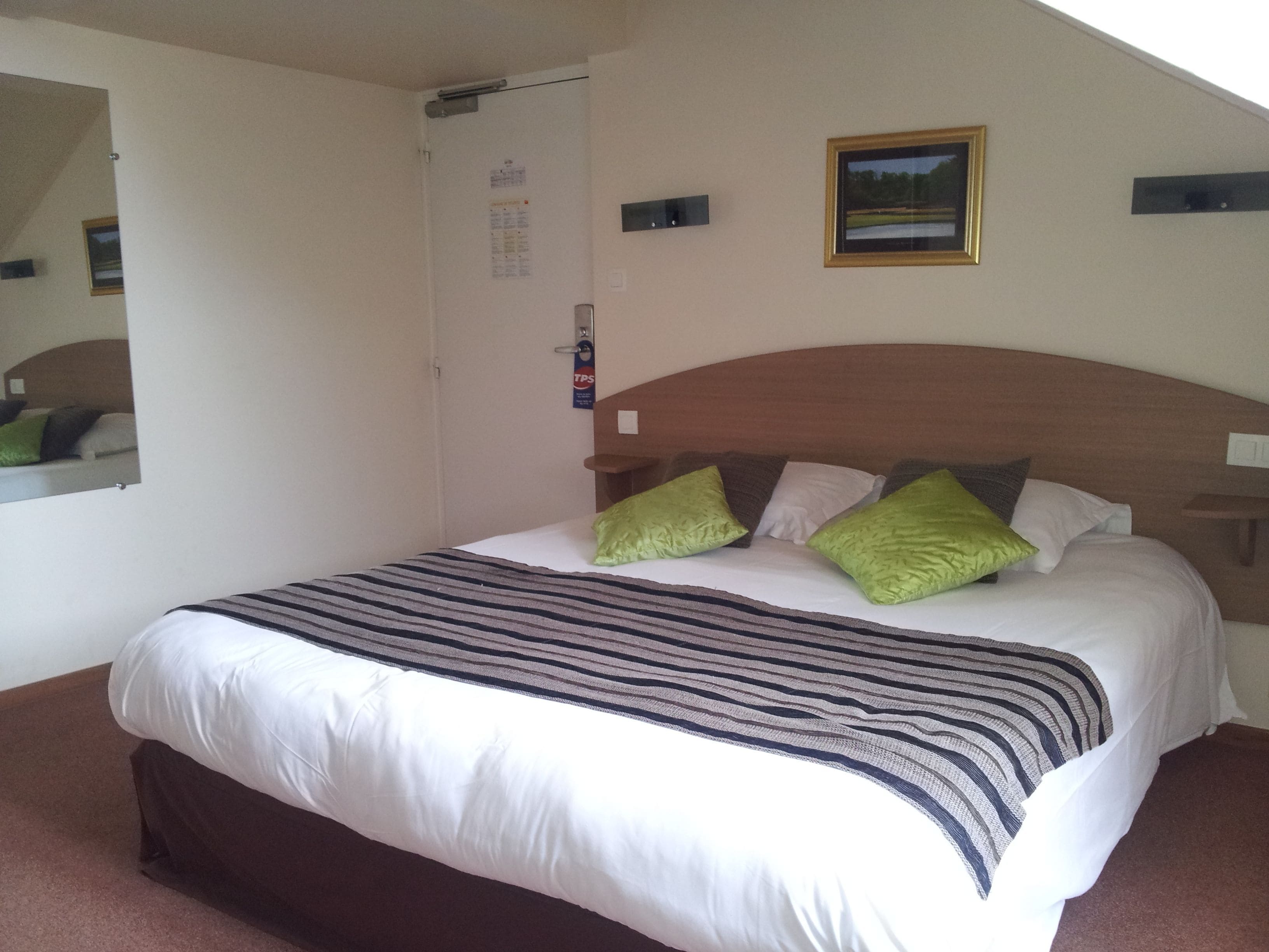 A hotel room with a large bed, a wooden headboard, and a single nightstand.