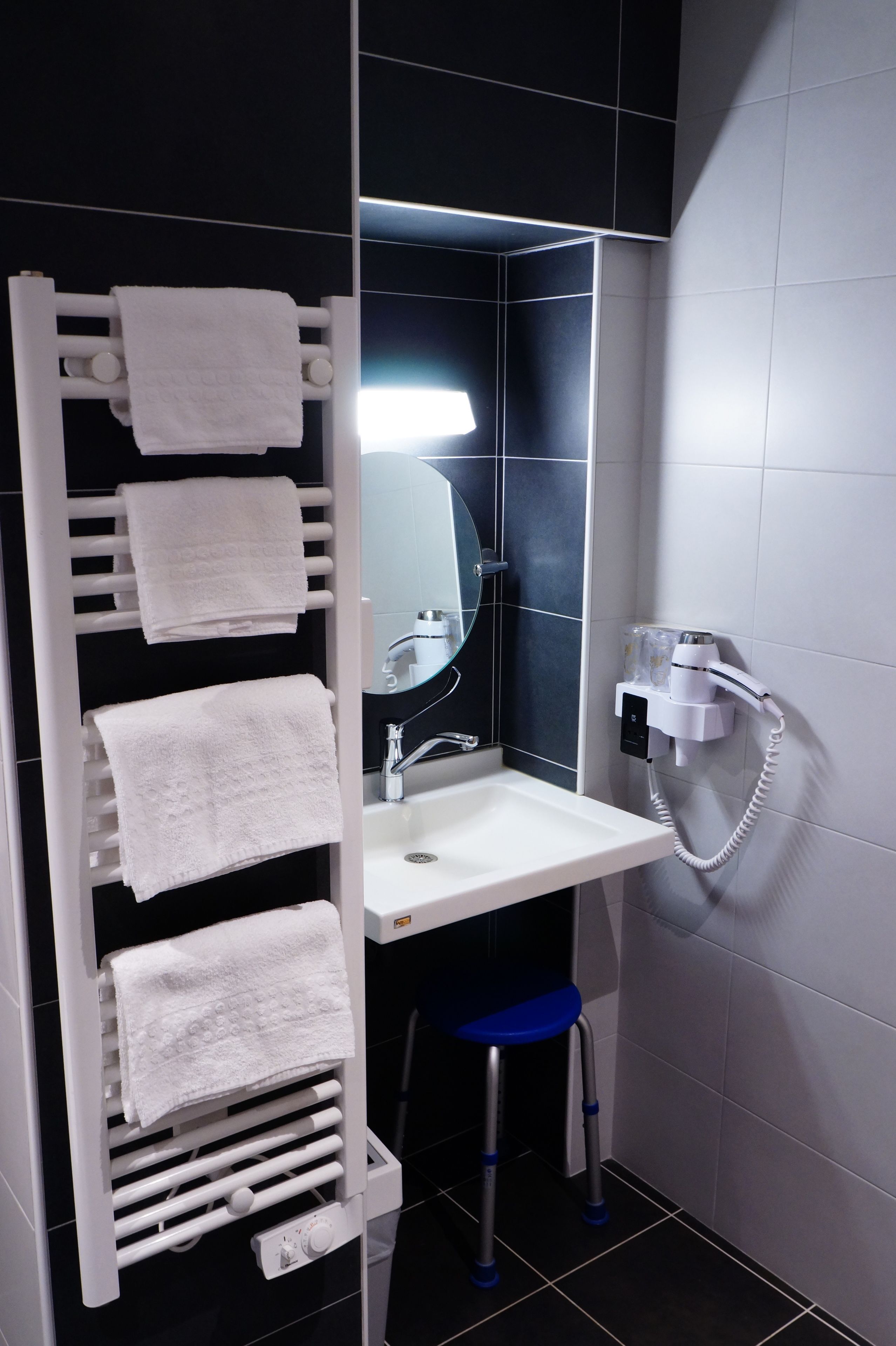 Een badkamer met een witte handdoekhouder, een wastafel, een spiegel en een haardroger op een wandmontage.