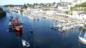 A harbor with numerous boats docked, a prominent red ship, and a town with buildings in the background. - Citotel Du Port Rhu (Douarnenez)