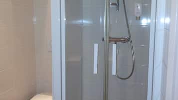 Una ducha con cerramiento de vidrio, cabezal de ducha manual y llave de agua manual.