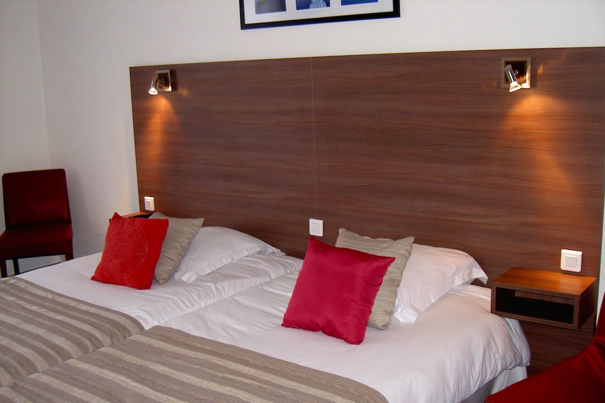A double bed with a wooden headboard, two bedside tables, and red and beige pillows.