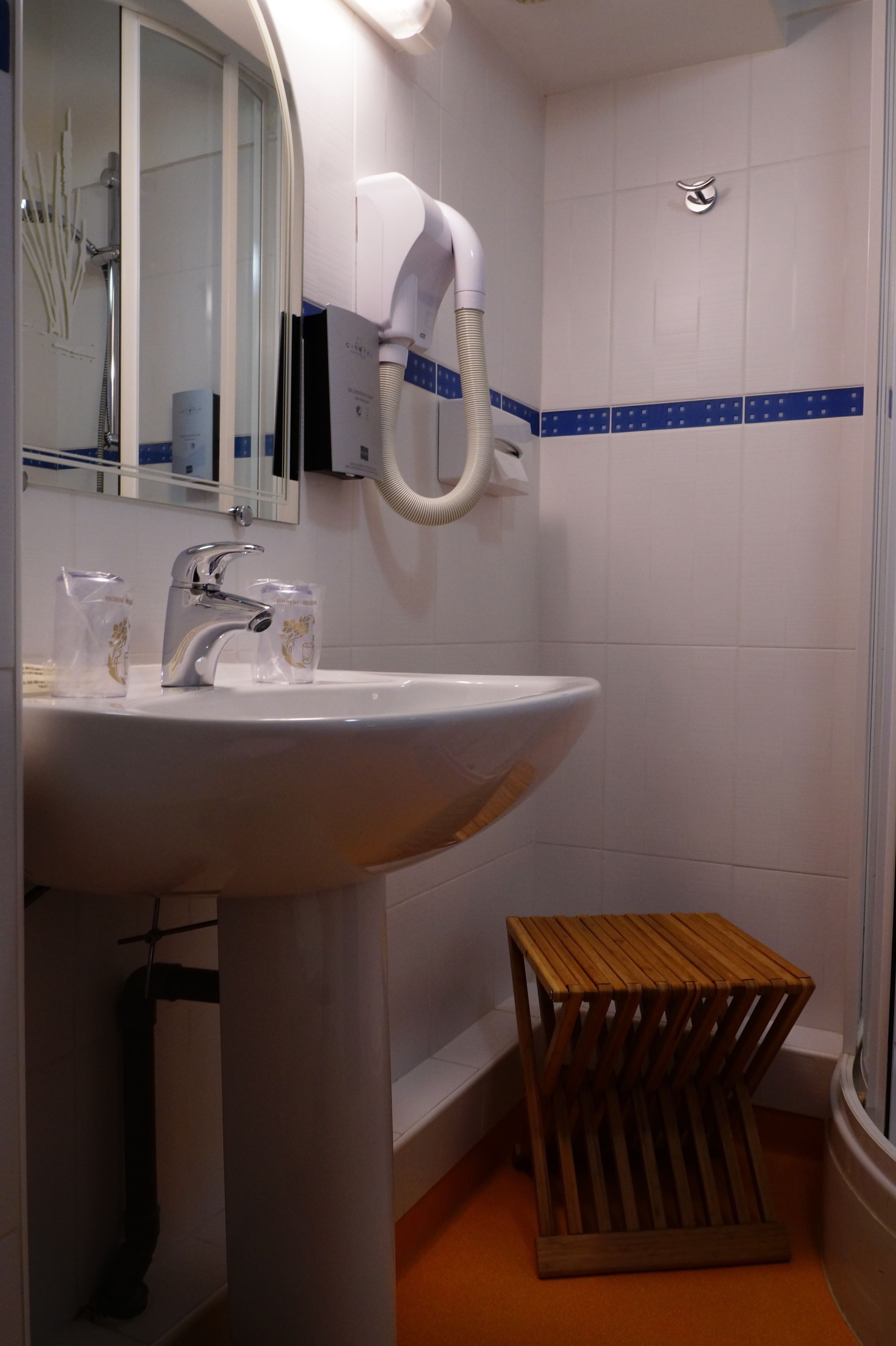 A bathroom with a white sink, a mirror, a hairdryer, and a wooden stool.