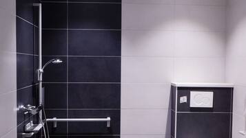 A modern bathroom with dark tiles, a shower, a toilet, and a hand dryer.