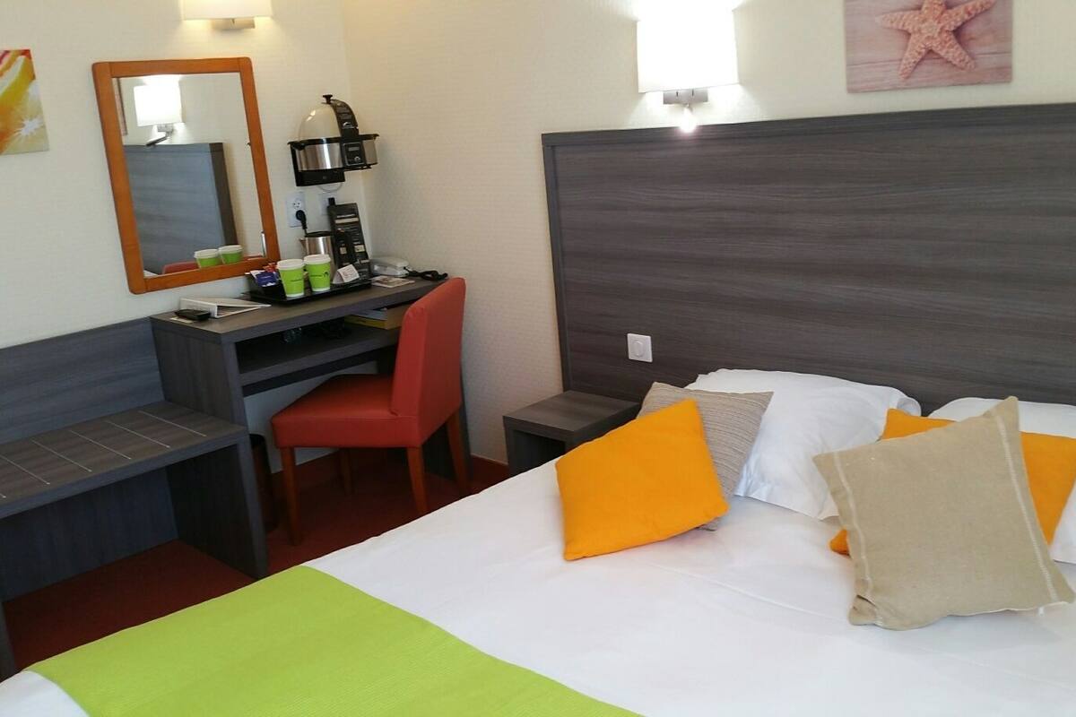 A hotel room with a bed, a desk, a chair, and a coffee machine.