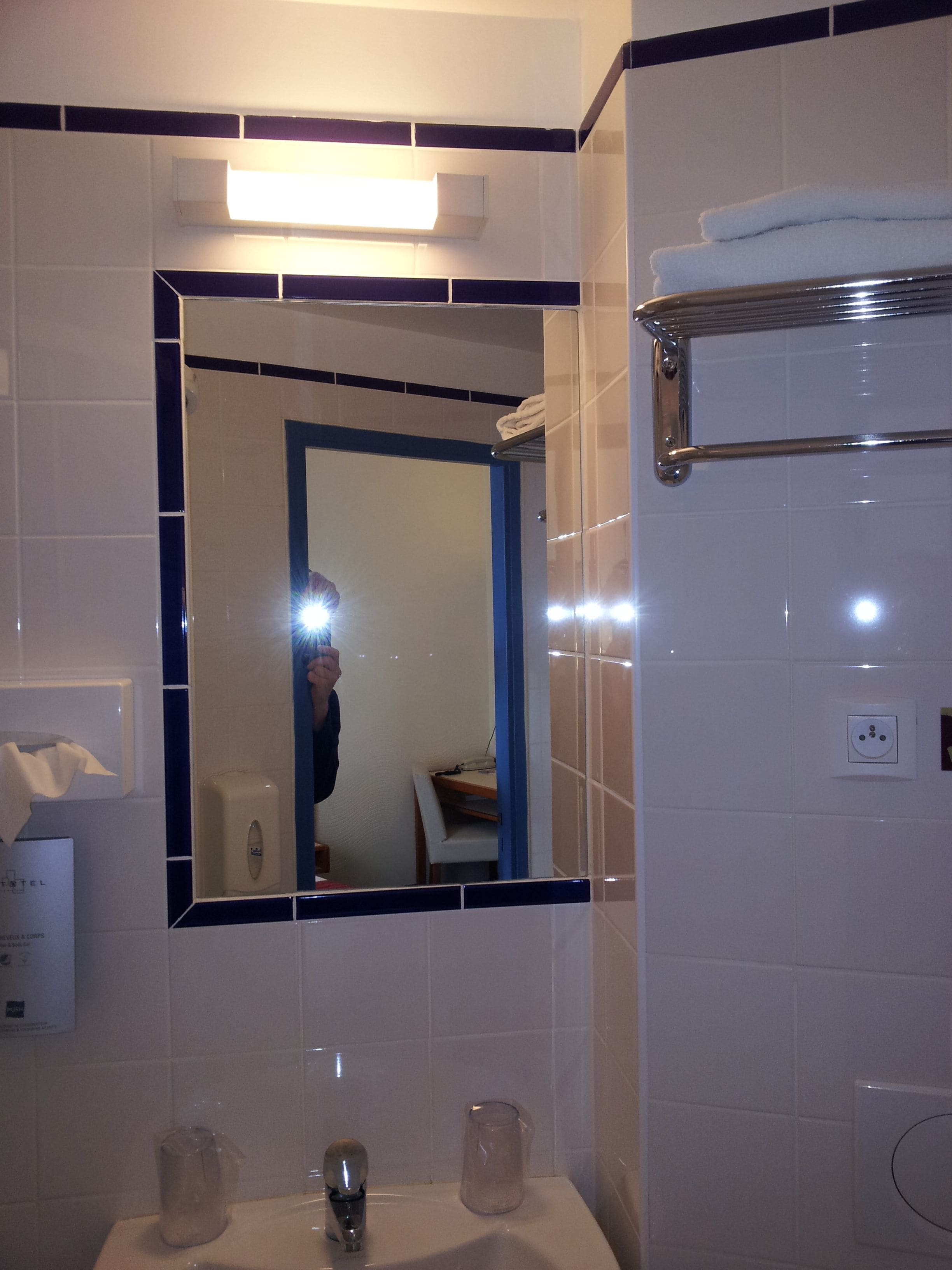 Un baño con espejo, lavabo y toallero.