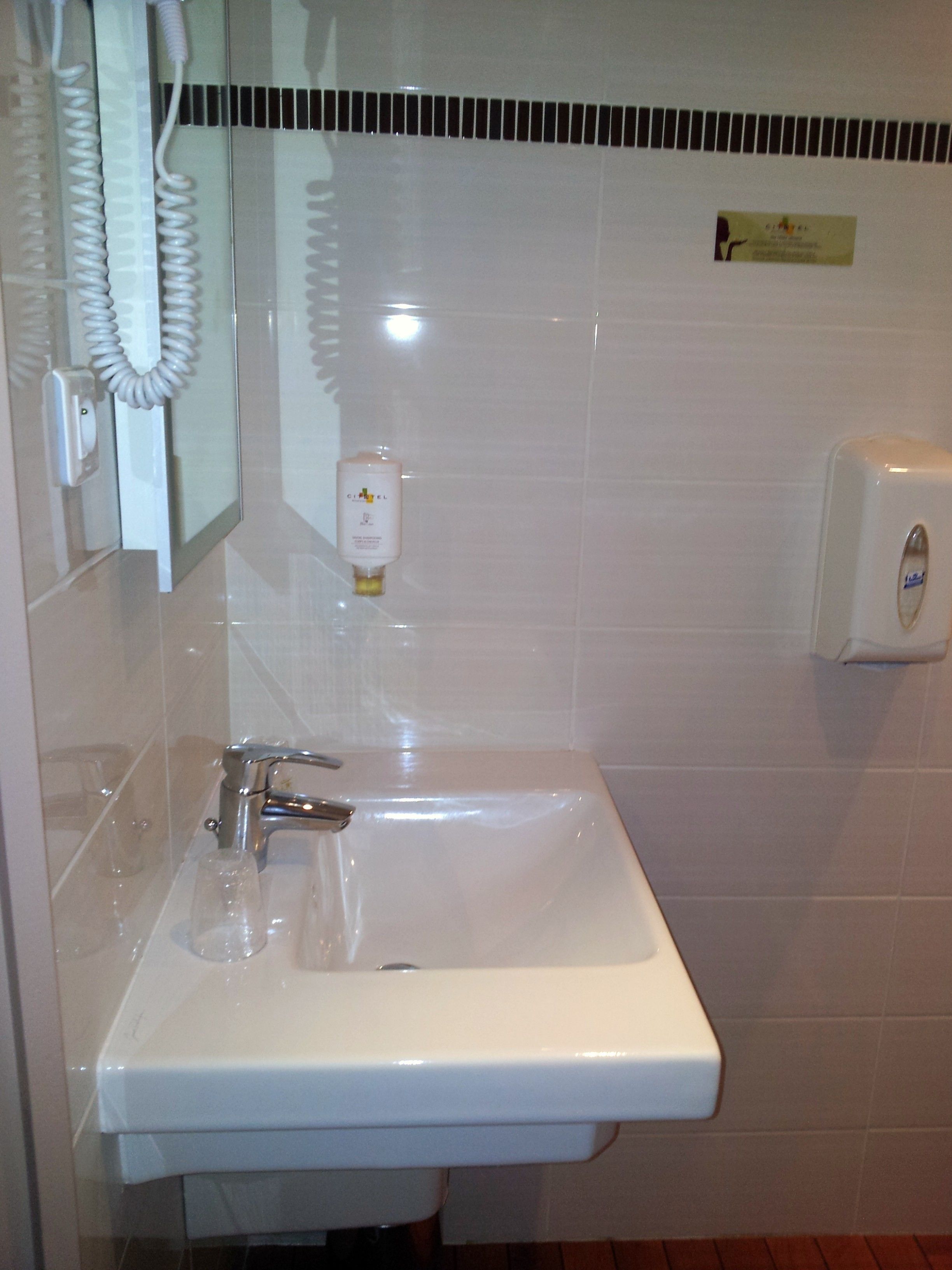 A bathroom with a white sink, a mirror, a hand dryer, and a soap dispenser.