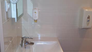 A bathroom with a white sink, a mirror, a hand dryer, and a soap dispenser.