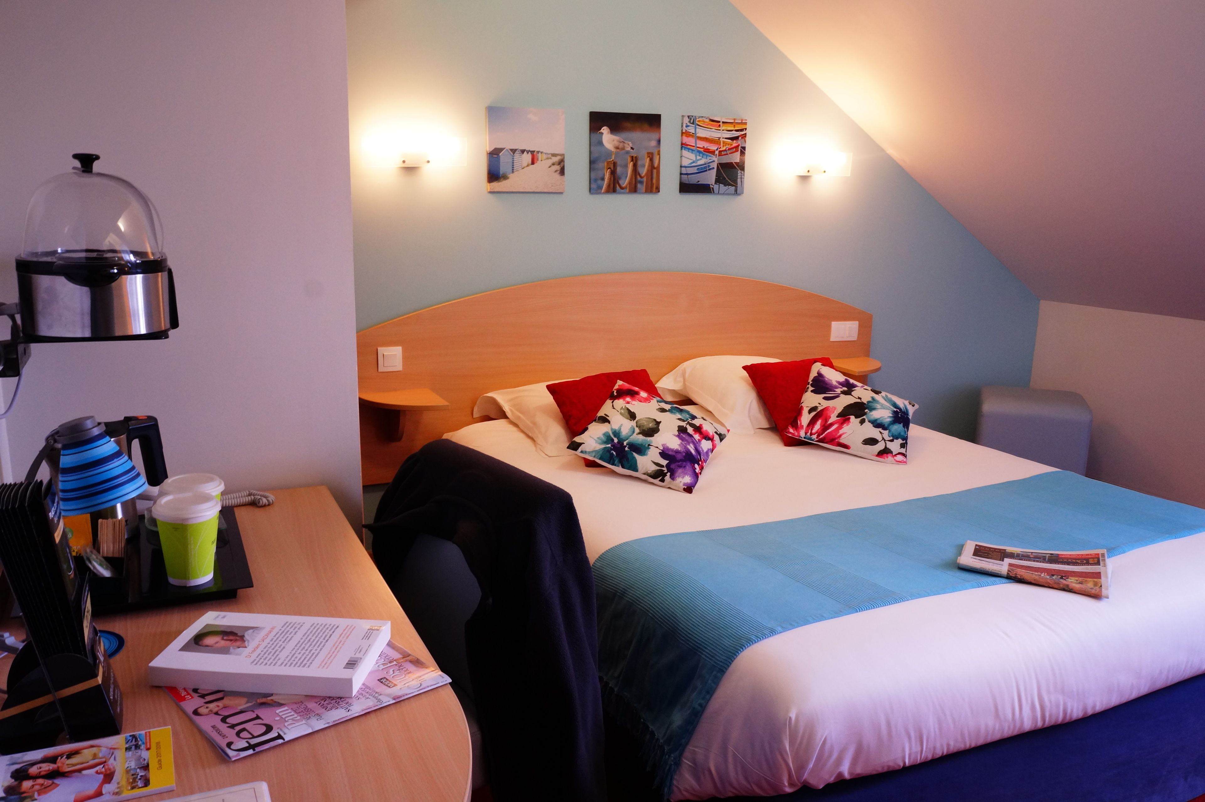Une chambre d’hôtel avec un lit, un bureau, une machine à café et un mur orné de trois tableaux.