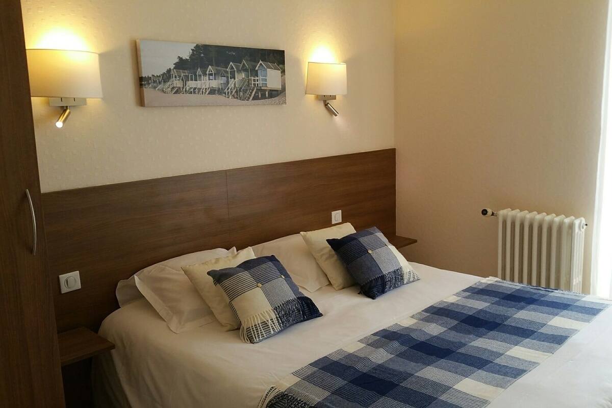 A neatly made bed with a checkered blanket, two pillows, and a headboard. There are two wall-mounted lamps and a framed picture above the bed.
