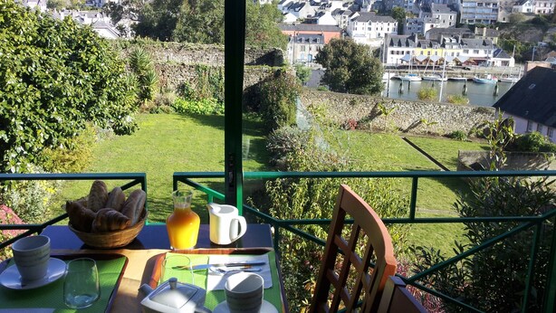 A table set with breakfast items, a view of a town with buildings and a church tower, and a stone wall in the foreground. - Citotel Du Port Rhu (Douarnenez)