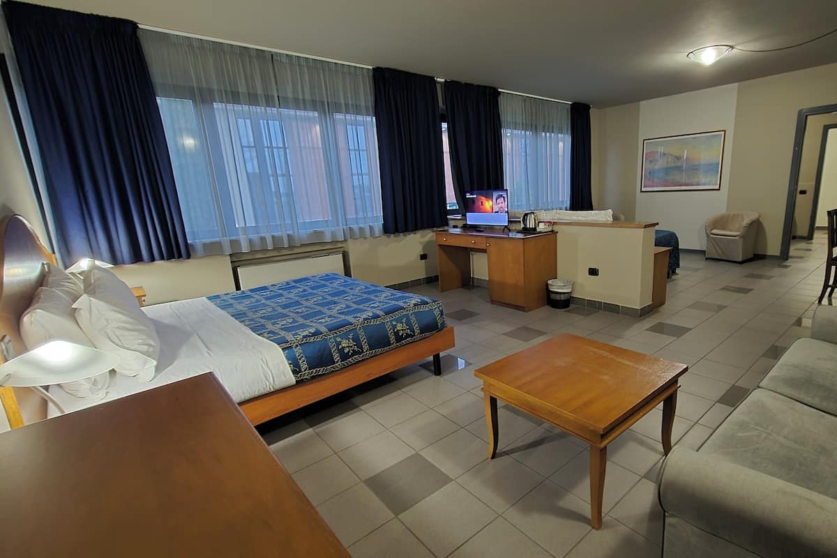 A hotel room with a bed, a desk, a sofa, and a small table.
