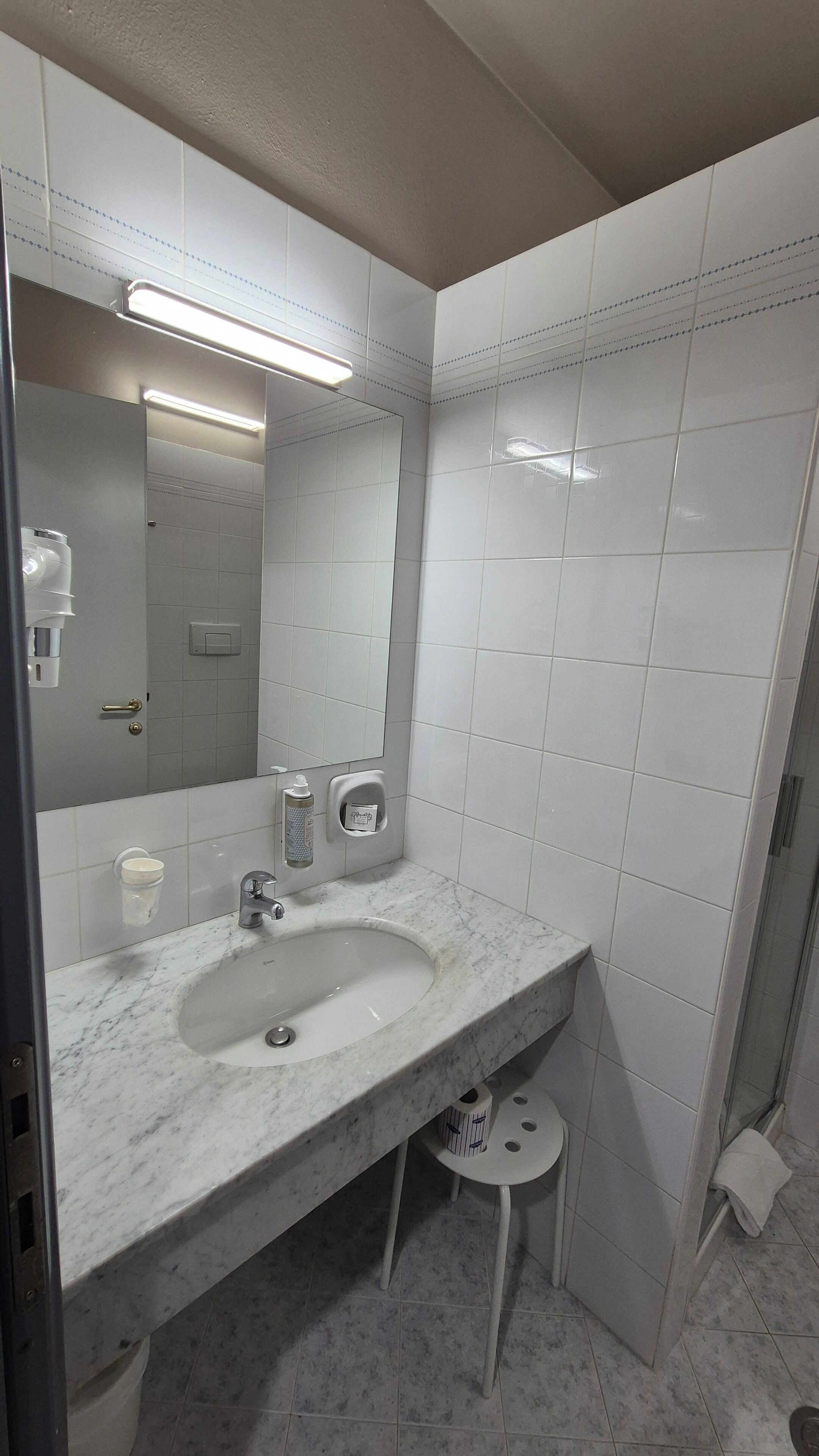 Un baño con lavamanos de mármol, espejo, inodoro y zona de ducha.