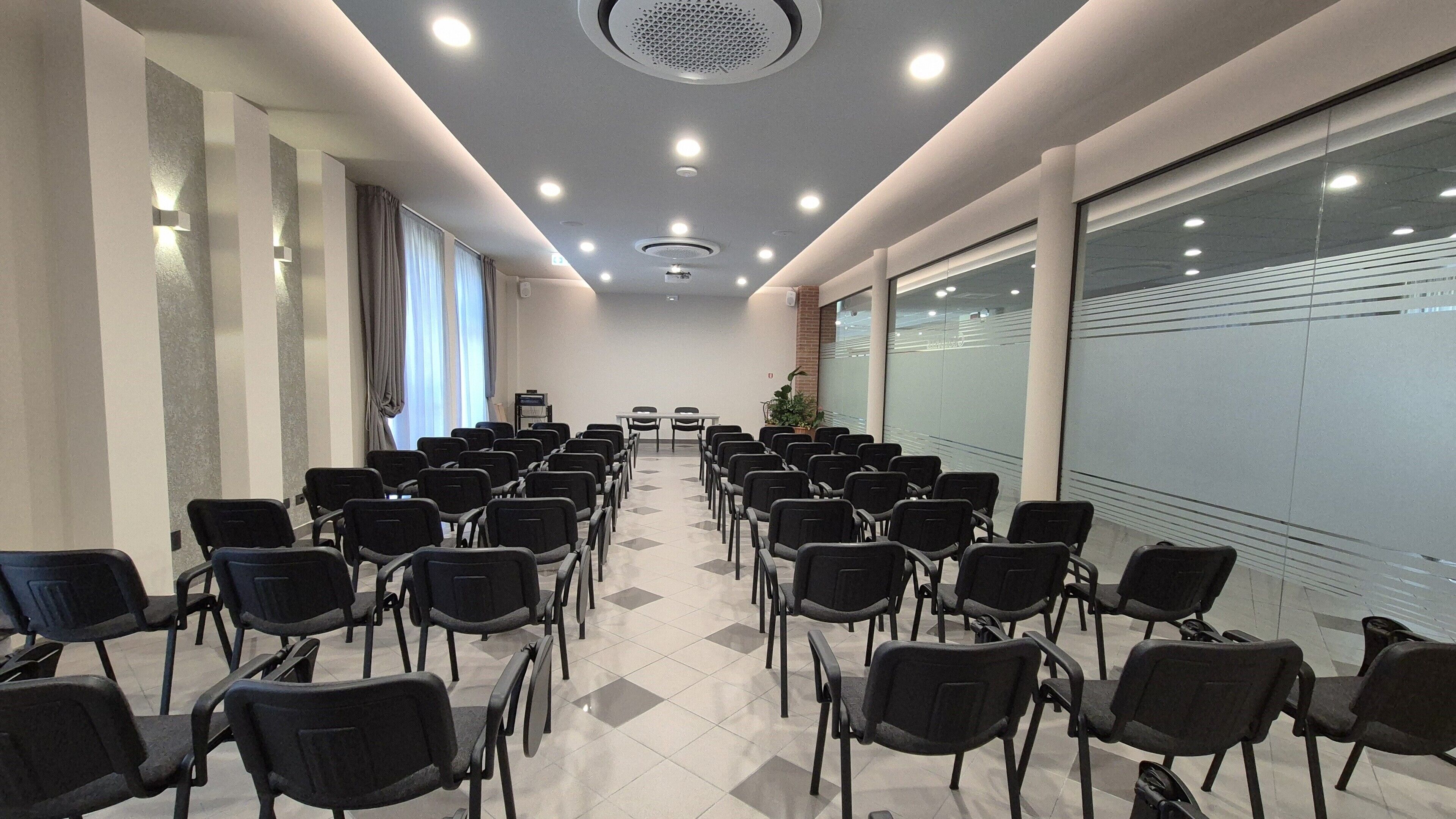 Un salón de conferencias con hileras de sillas, una pantalla de proyector y un ventanal grande.