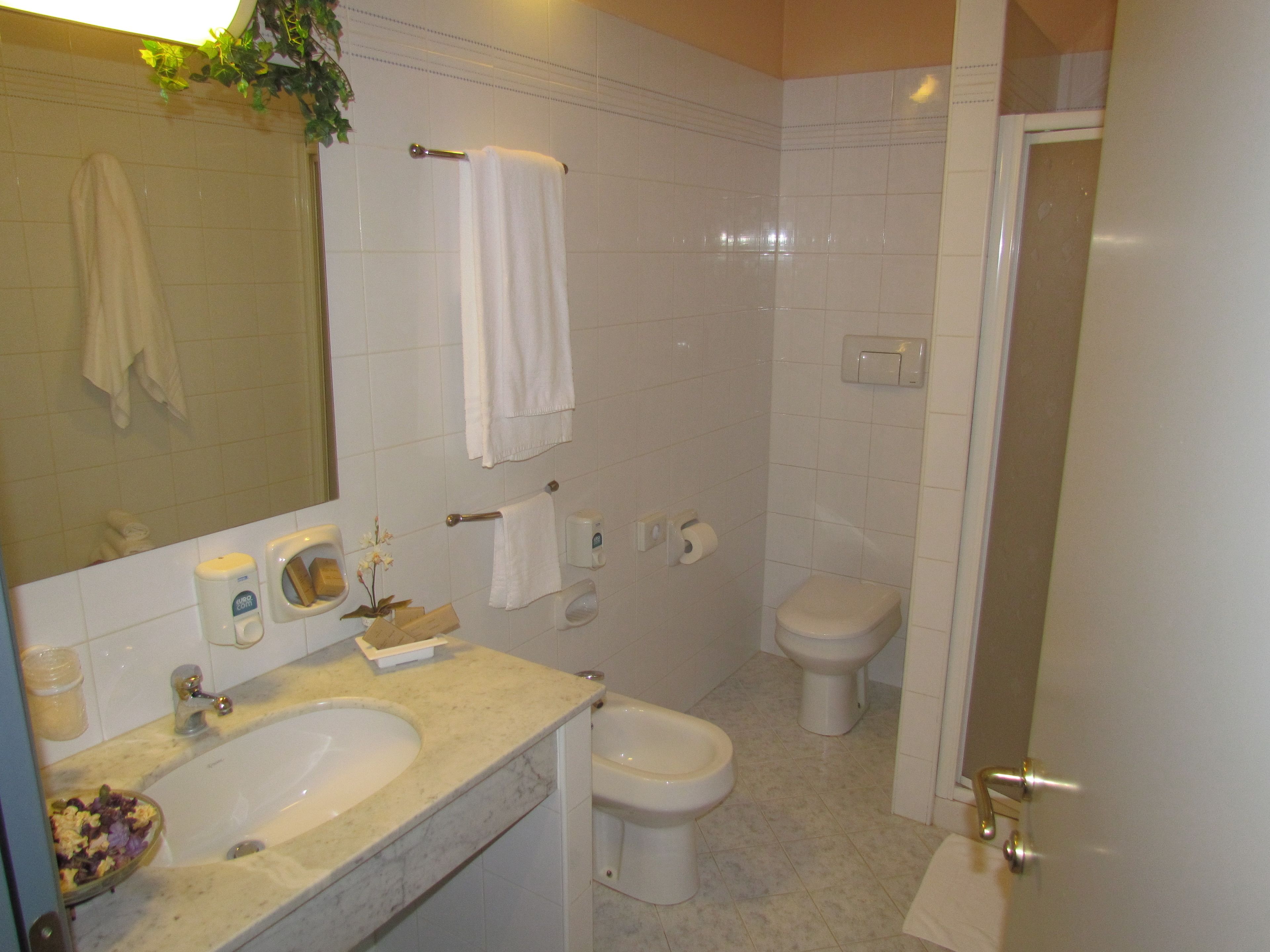 Ein Badezimmer mit Waschbecken, Toilette und Bidet. Handtücher hängen an der Wand, es gibt einen Seifenspender und einen Toilettenpapierhalter.