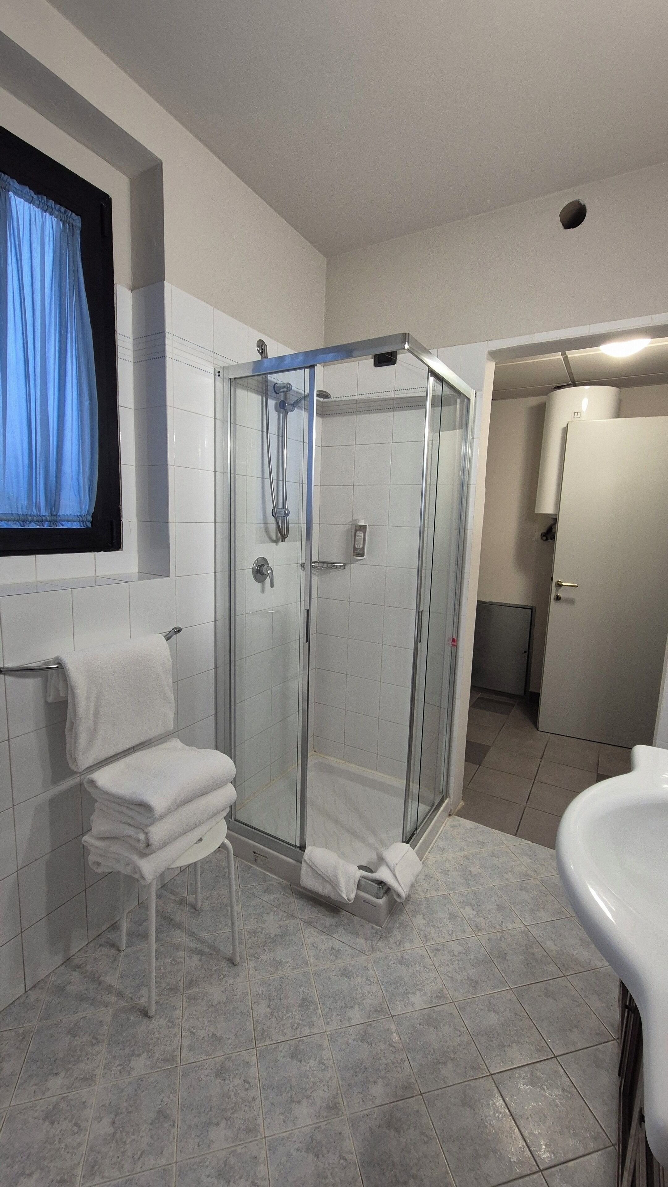 Un baño moderno con ducha de vidrio, un lavamanos blanco y un perchero.