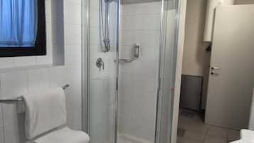 Un baño moderno con ducha de vidrio, un lavamanos blanco y un perchero.