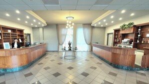 A reception area with a marble floor, two reception desks, a chandelier, and a coffee machine. - Hotel Le Cerbaie (Altopascio)