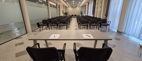 A conference room with a long table and chairs, large windows with curtains, and a tiled floor.