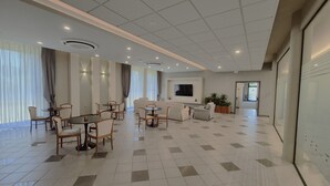 A spacious living area with a sofa, dining table, and chairs, a flat-screen TV mounted on the wall, and a potted plant. - Hotel Le Cerbaie (Altopascio)