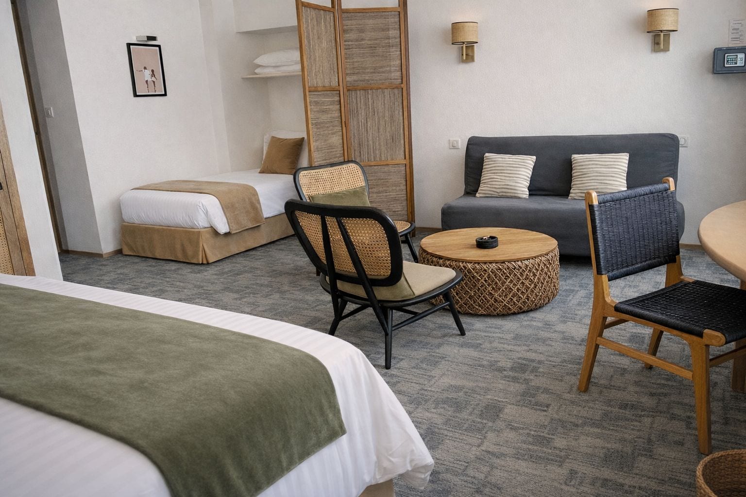 Ein Hotelzimmer mit einem Bett, einem Sofa, einem Esstisch und einem Stuhl. An der Wand befinden sich Wandlampen und ein Bilderrahmen.