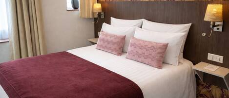 Habitación de hotel con cama, dos almohadas, mesita de noche, lámpara y un papel tapiz con diseño floral.
