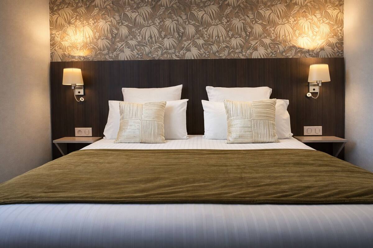 Una habitación de hotel con una cama grande, dos lámparas de noche, un papel tapiz estampado y un cabecero de madera.