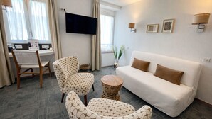 Een hotelkamer met een bank, twee gestreept fauteuils, een klein rond tafeltje, een televisie en een bureau met stoel.