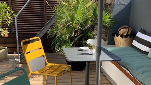 Een terras met een gele stoel, een tafel met een plant in pot en een bank met gestreepte kussens.