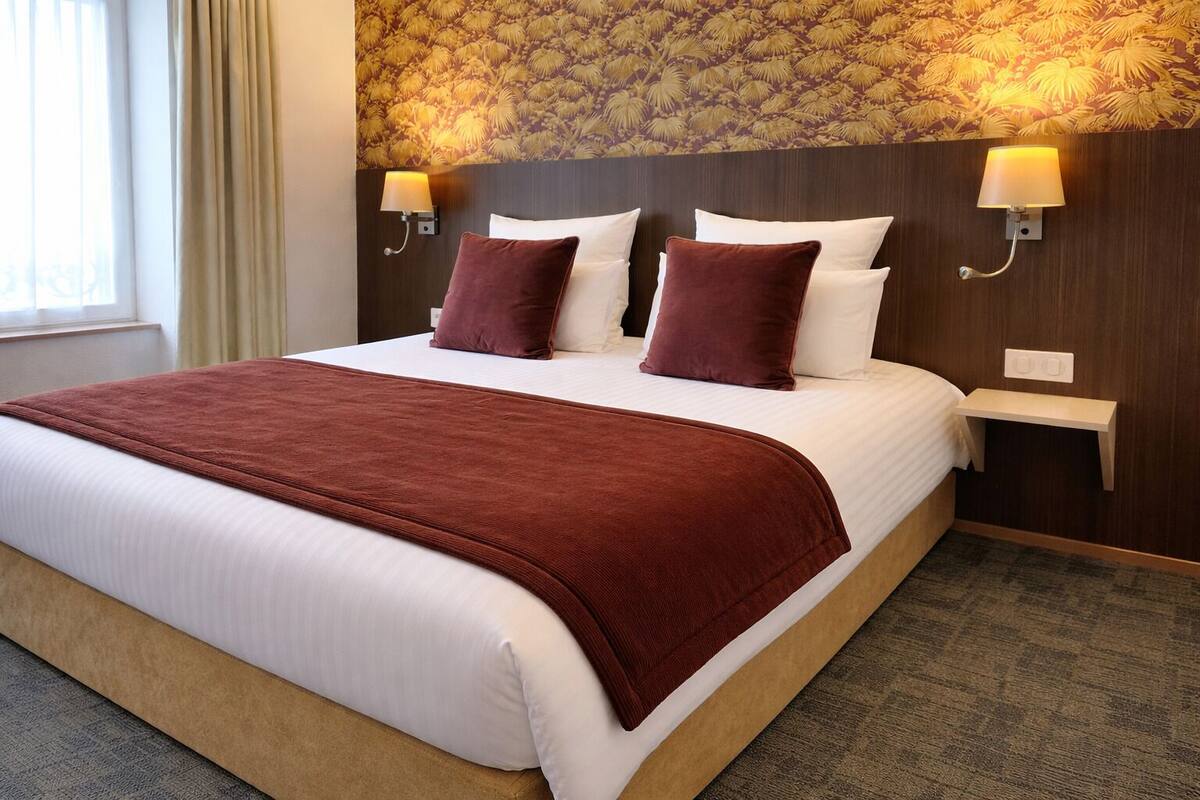 Habitación de hotel con una cama grande, dos lámparas de pared, una mesita de noche y un papel tapiz estampado.