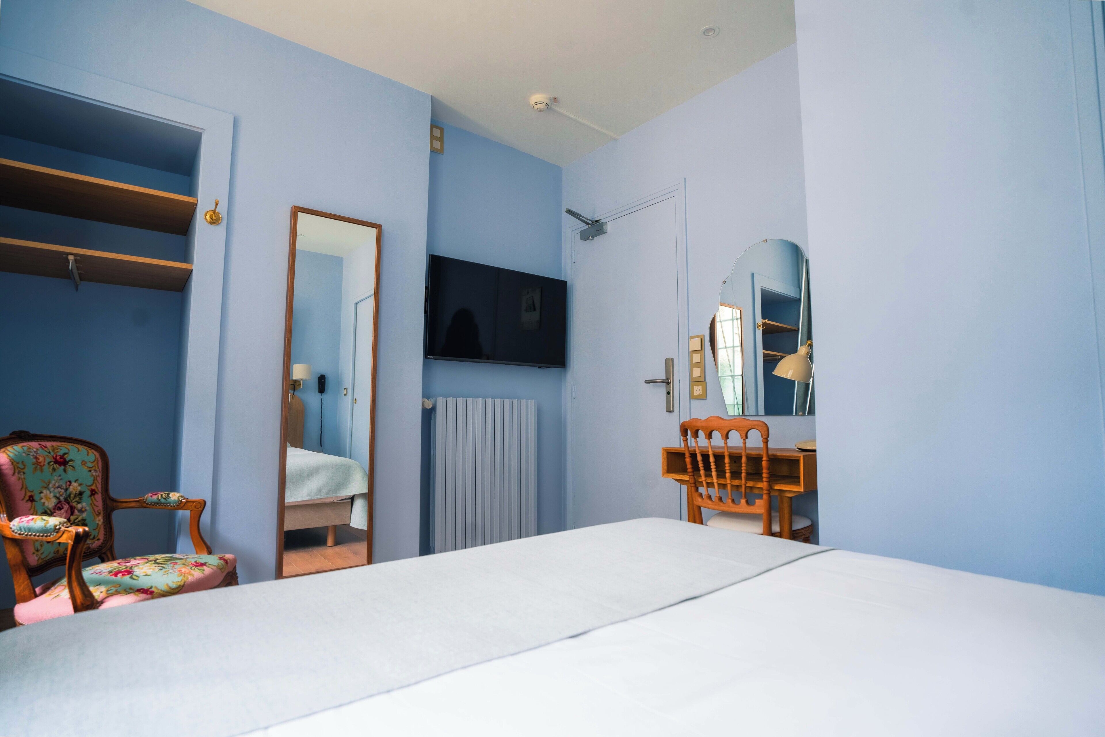 A bedroom with a bed, a wooden chair, a desk, a mirror, and a television.