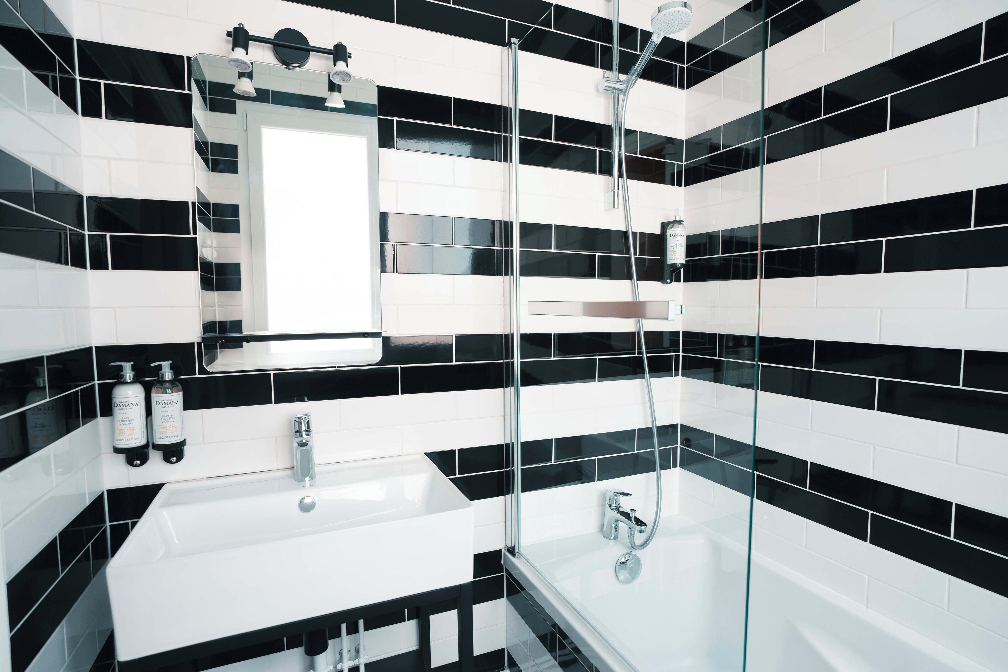 Une salle de bain moderne avec des carreaux noirs et blancs, une douche à parois de verre et deux lavabos.