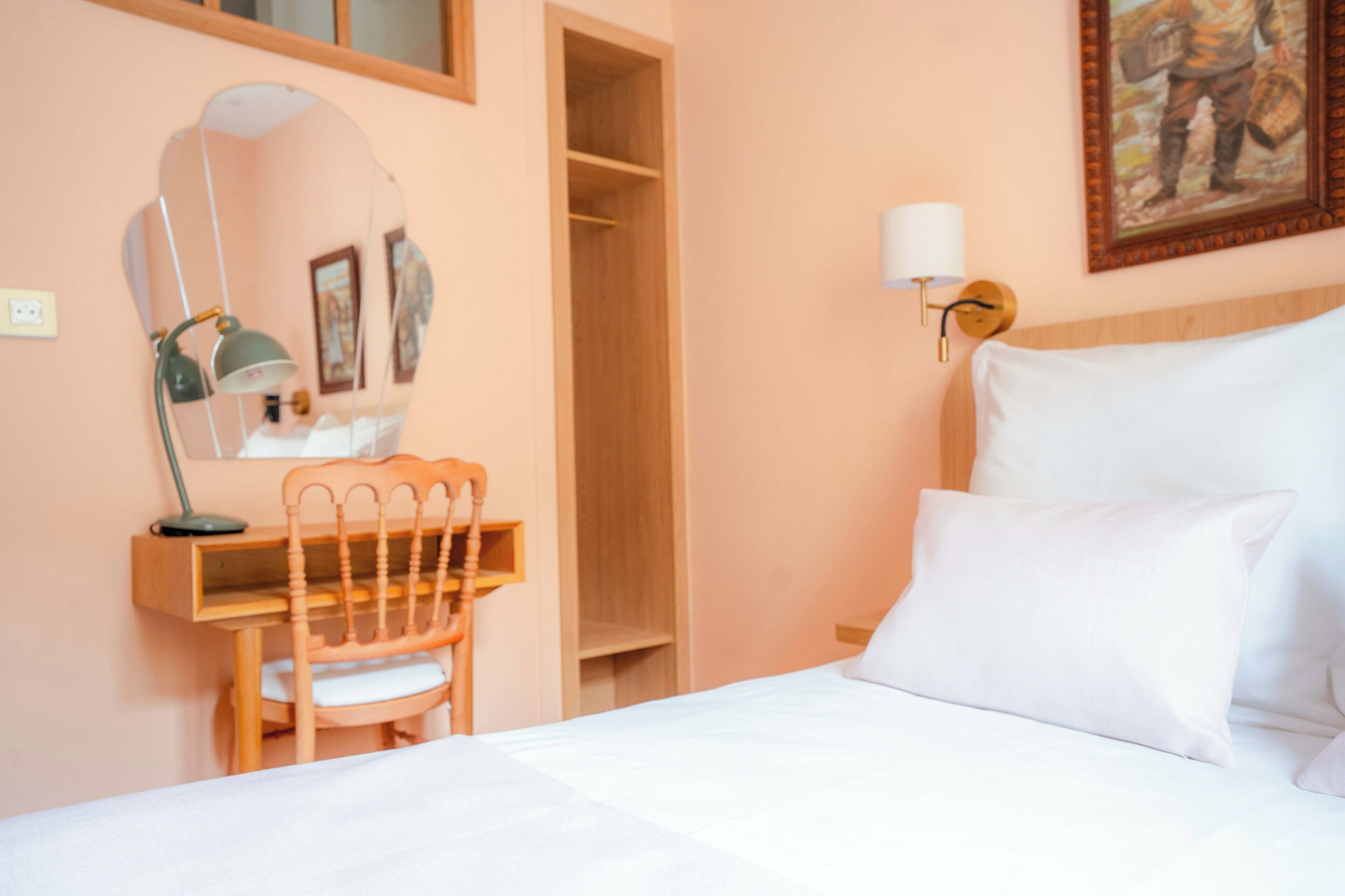 Une chambre à coucher avec un lit, un bureau avec une chaise, un miroir et une lampe fixée au mur.