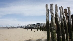 A sandy beach with wooden posts in the foreground and buildings in the background.