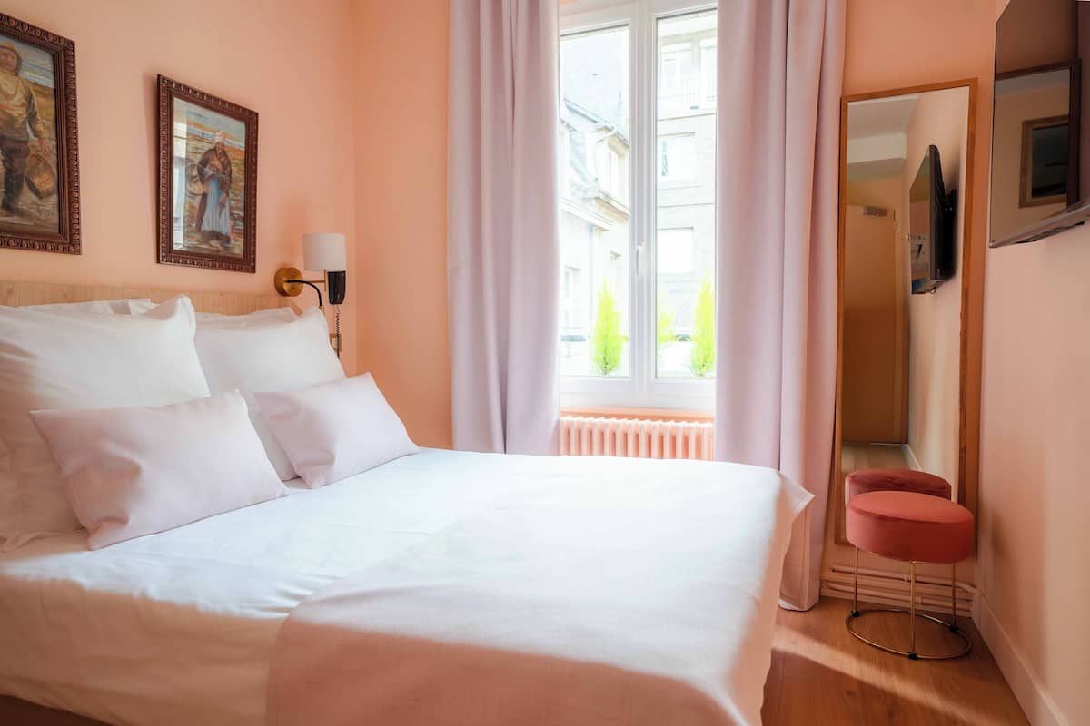 A hotel room with a large bed, a small round table, a mirror, and two paintings on the wall.