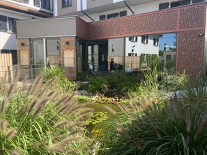 Ein modernes Haus mit einer Holzterrasse, einem kleinen Teich und üppiger Bepflanzung.