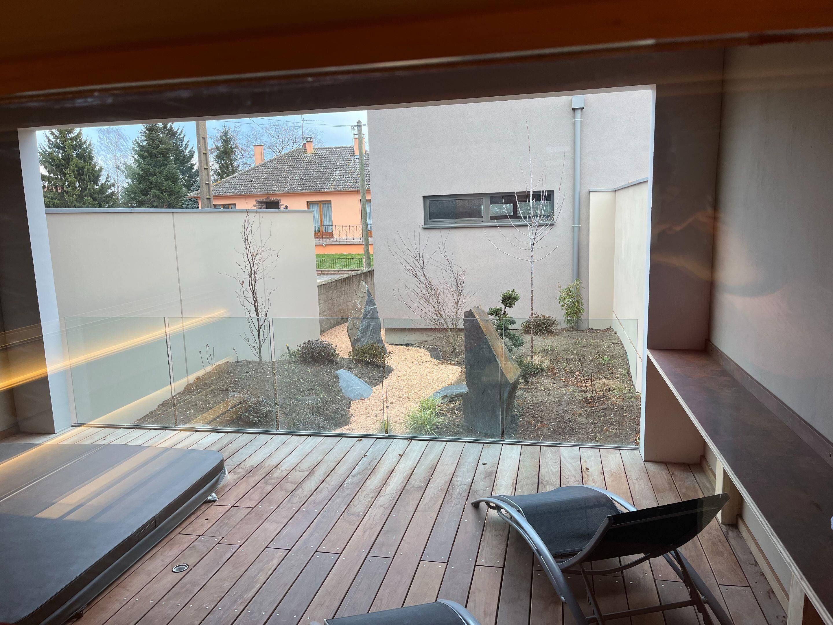 A balcony with a view of a backyard, a wooden deck, and a chair.