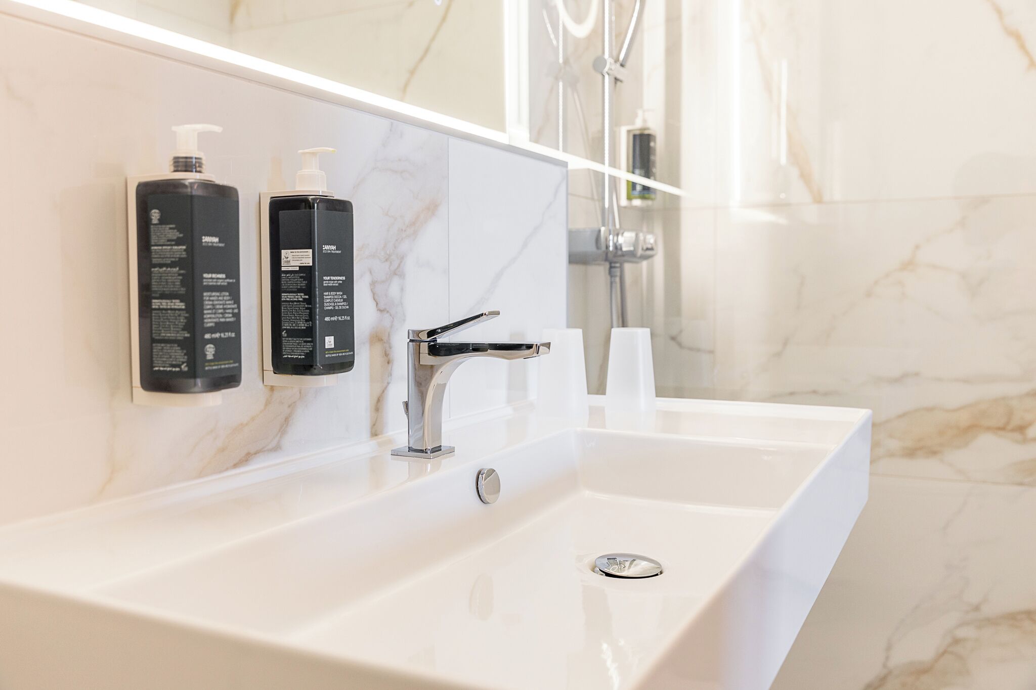Een moderne badkamer met een witte wasbak, twee zwarte toiletartikelen en een grote spiegel.