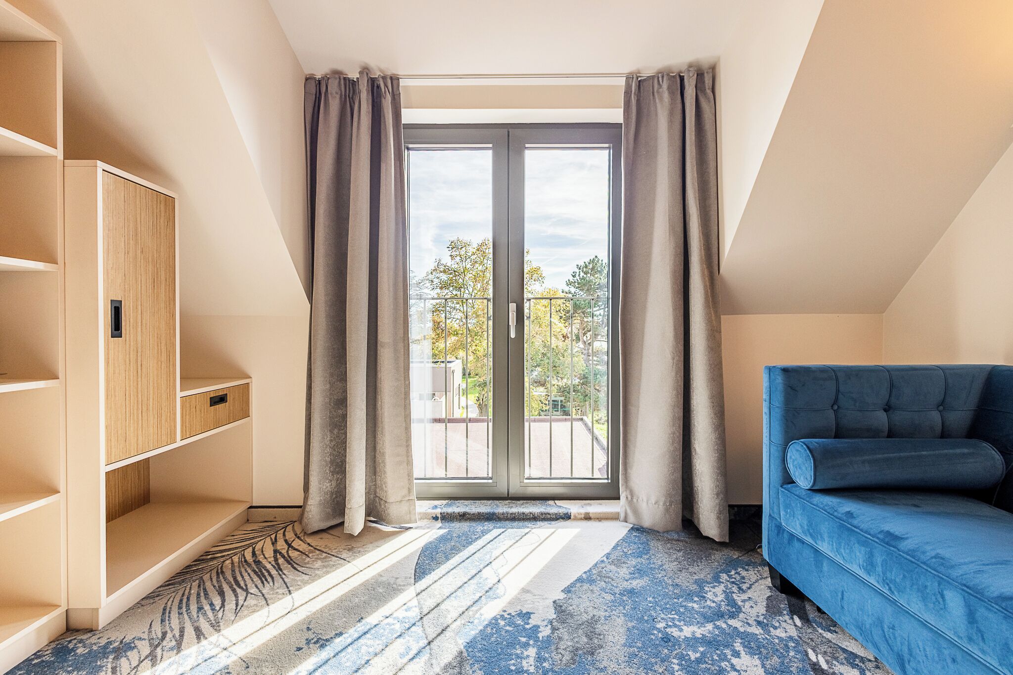 A room with a blue sofa, a wooden cabinet, and a large window with curtains.
