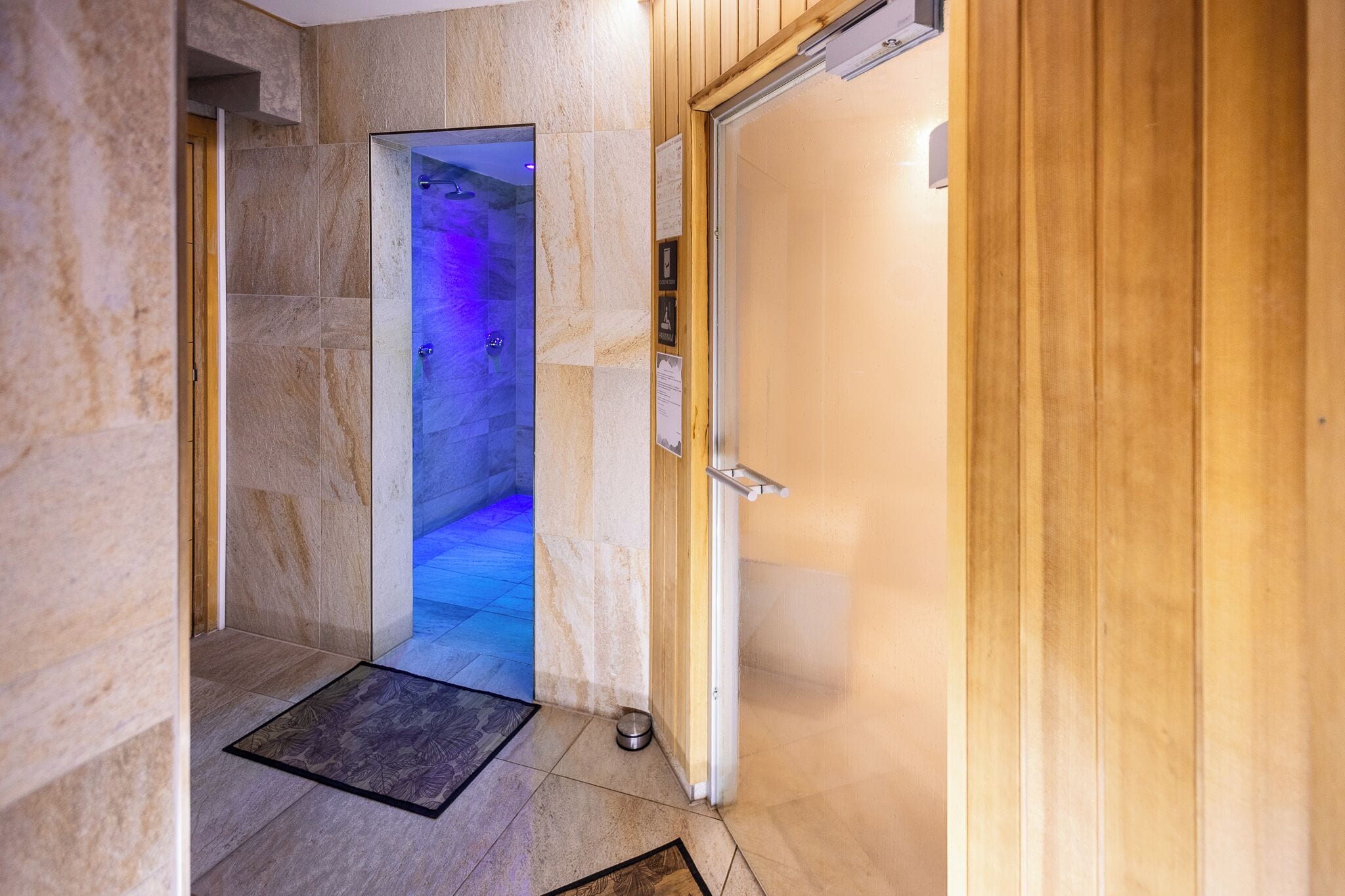 A hallway leading to a spa room with a wooden door and a tiled floor.
