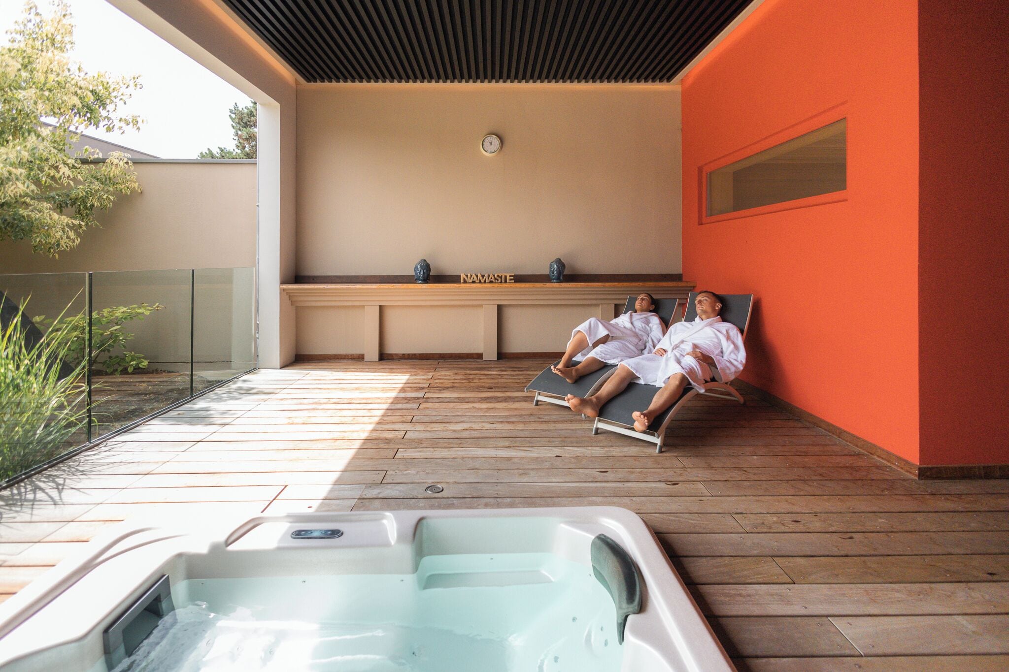 A spa area with a hot tub, wooden deck, and a wall with a clock.