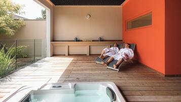A spa area with a hot tub, wooden deck, and a wall with a clock.