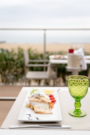 Una mesa de comedor con un plato de comida, un vaso verde y vistas a la playa.