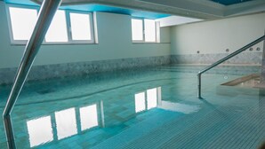 Piscina interna com água cristalina, piso ladrilhado e corrimãos de metal.