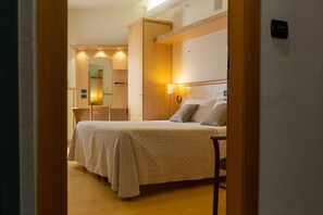 Habitación de hotel con cama, escritorio y silla. Se observa un espejo y una lámpara en la pared.