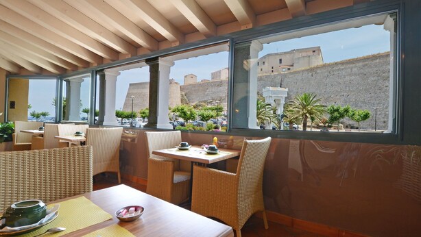 Ein Restaurant mit Korbmöbeln und großen Fenstern mit Blick auf eine historische Festung.